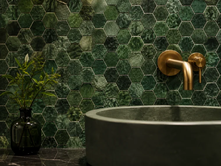 Deep green hexagonal mosaic wall behind a stone basin with a brushed brass tap.